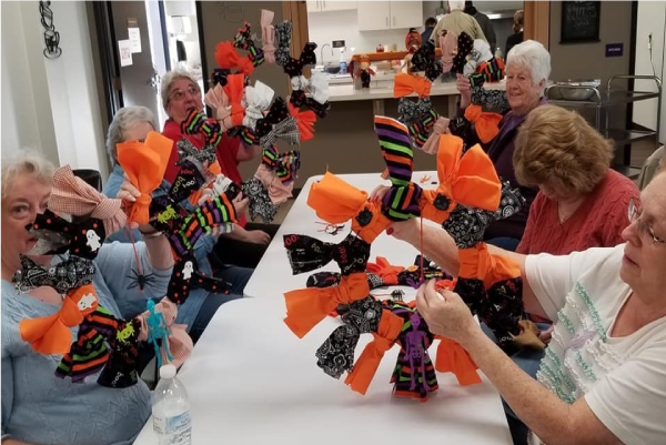 Picture of a group of 6 women sitting at a table and presenting crafts at the Senior Center