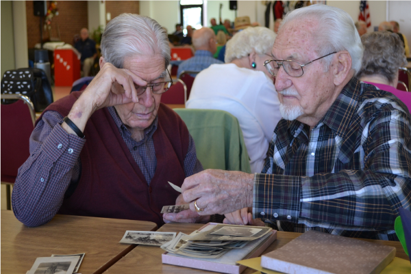 Picture of a large group of people sitting at tables and viewing photographs at the Senior Center