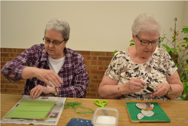Picture of 2 women sitting in chairs working on a project at the Senior Center